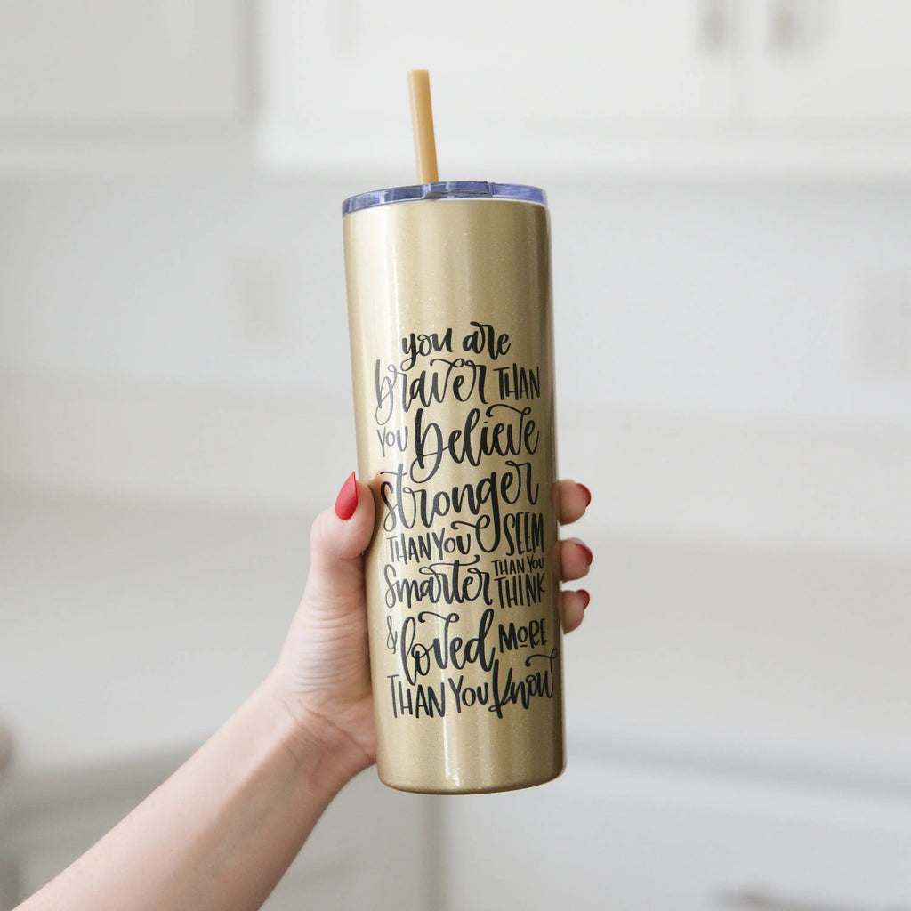 Gold glitter skinny tumbler with straw, black motivational quote on front, held in hand