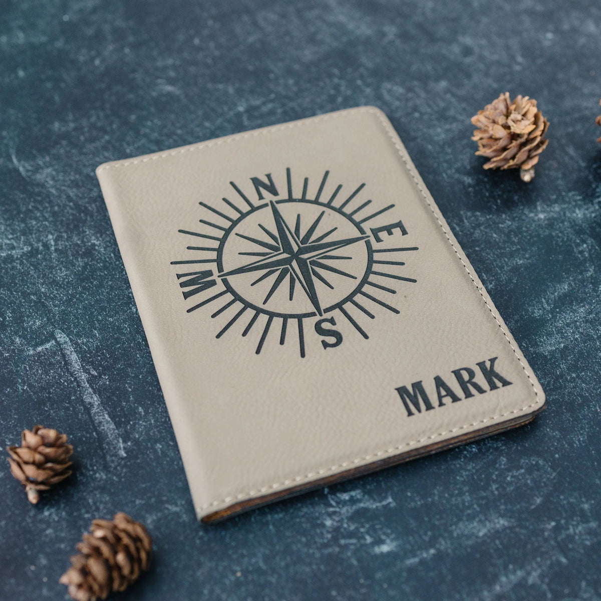 Gray faux leather passport holder with compass emblem and 'MARK' engraving.