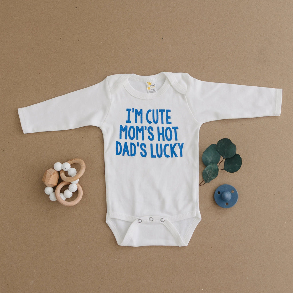 White long-sleeve baby bodysuit with blue “I’m cute mom’s hot dad’s lucky” text