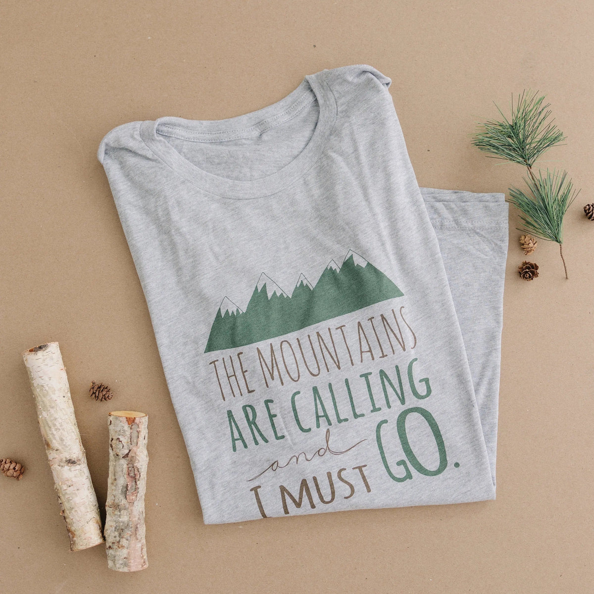 Folded gray crewneck unisex t-shirt with mountain graphic and "The Mountains are Calling"