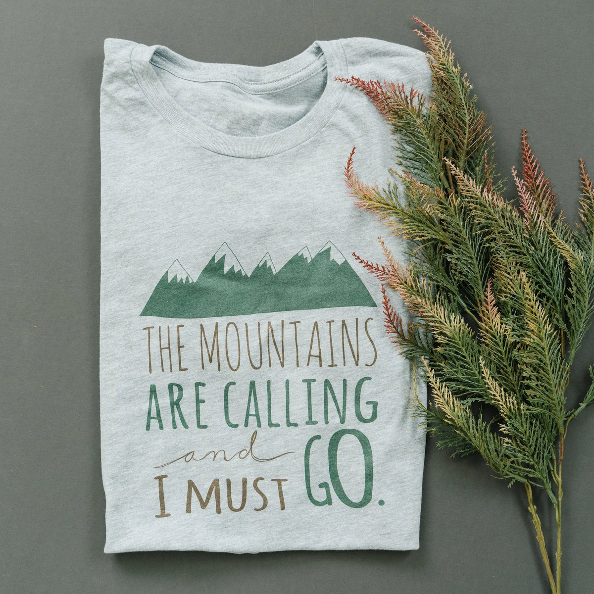 Gray crewneck unisex t-shirt featuring mountain range graphic and "I must go" phrase