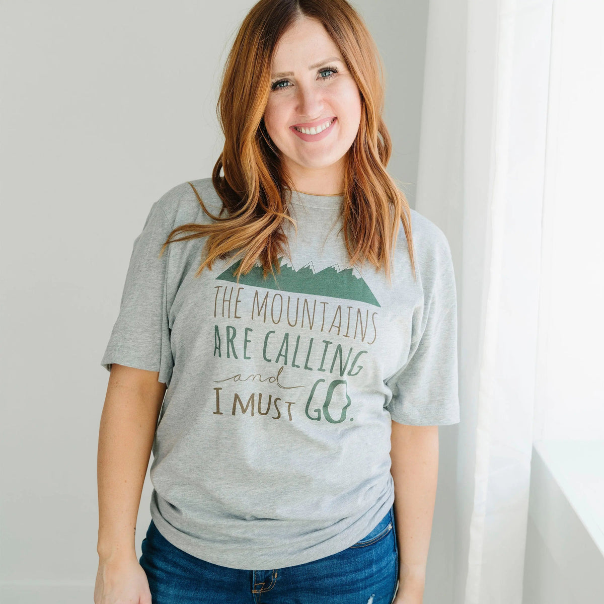 Gray crewneck unisex t-shirt with green mountain print and "I must go" lettering