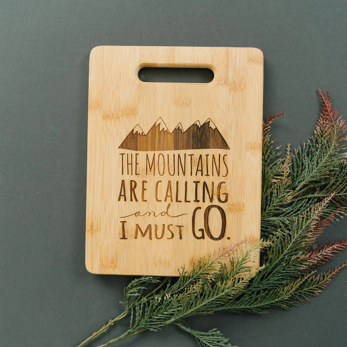 Bamboo cutting board with handle cutout, mountain skyline, and quote "The mountains are calling"