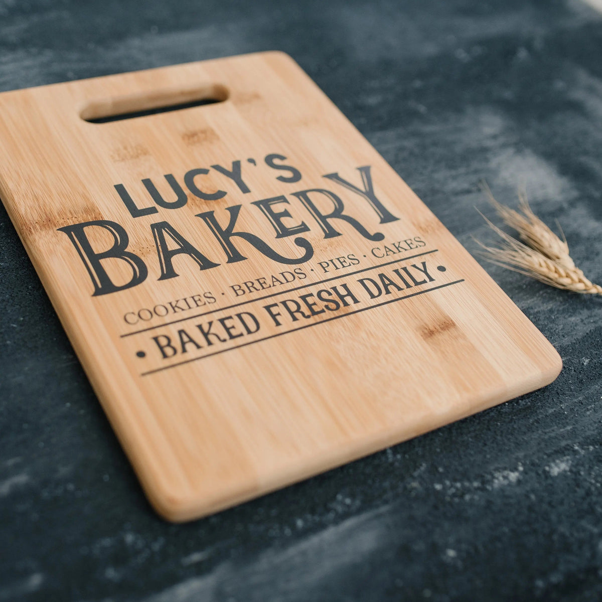 Light wood cutting board with handle, diagonal 'LUCY'S BAKERY' text