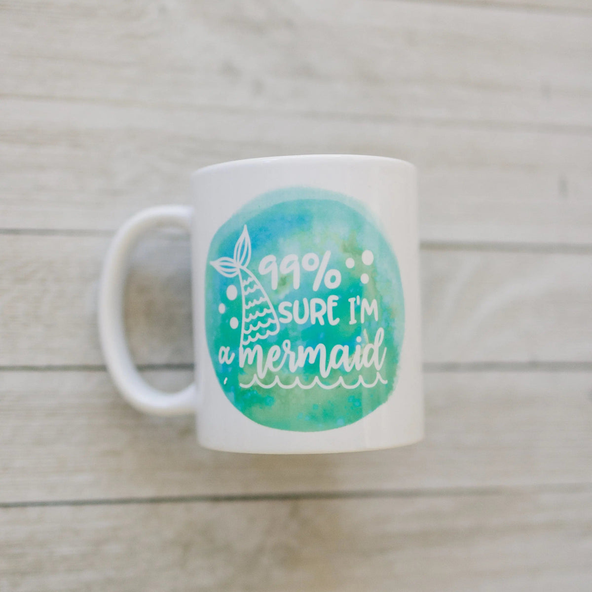 White ceramic mug with teal mermaid watercolor graphic and '99% sure I'm a mermaid' text