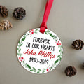 Round memorial ornament with red ribbon, floral border, name and dates: John Phillip 1950–2019