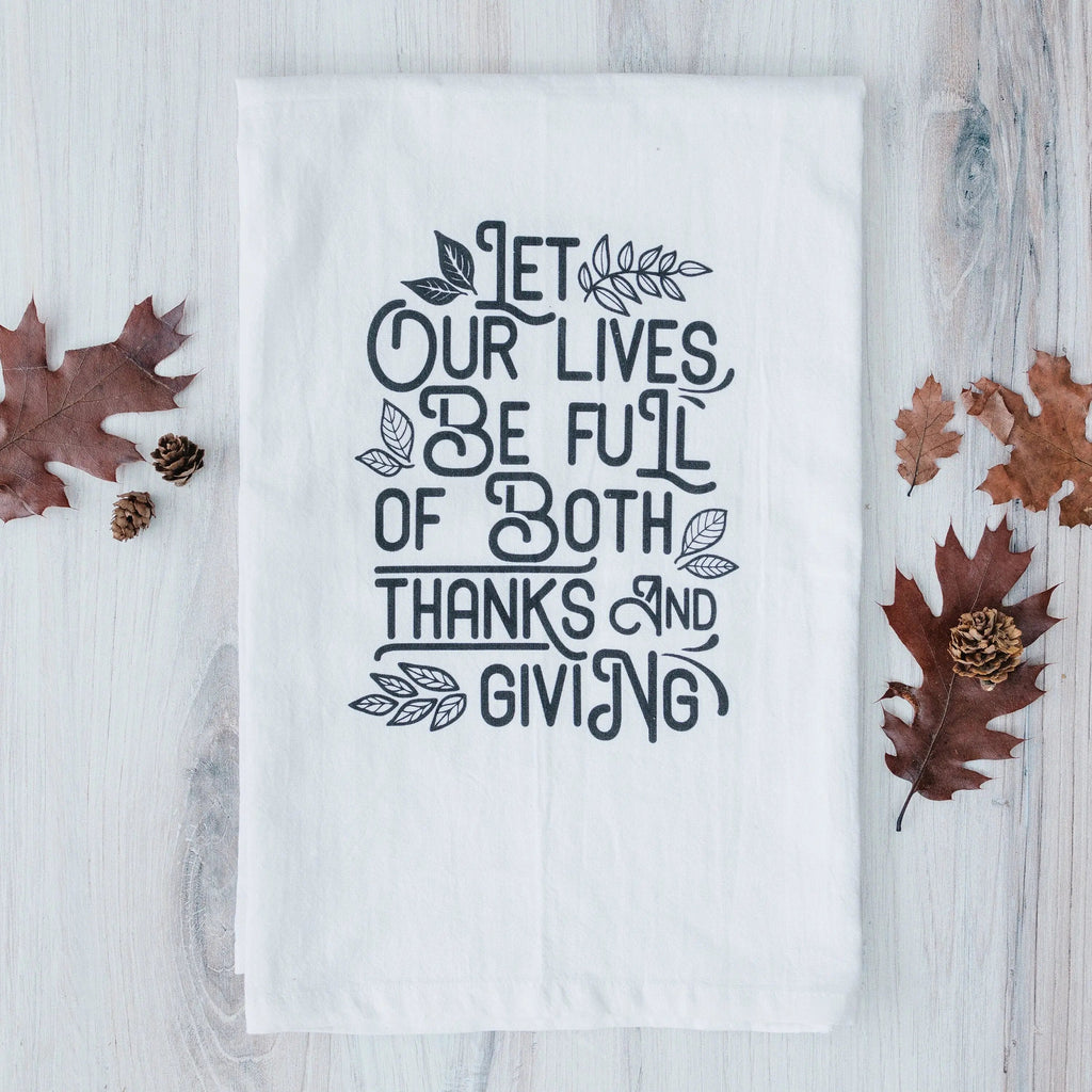 White Thanksgiving kitchen towel with black quote, laid flat on light wood