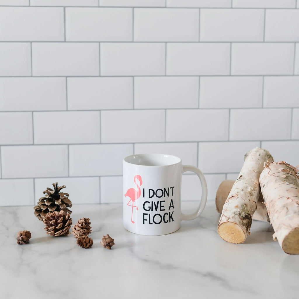 White ceramic coffee mug featuring pink flamingo and 'I DON'T GIVE A FLOCK' text