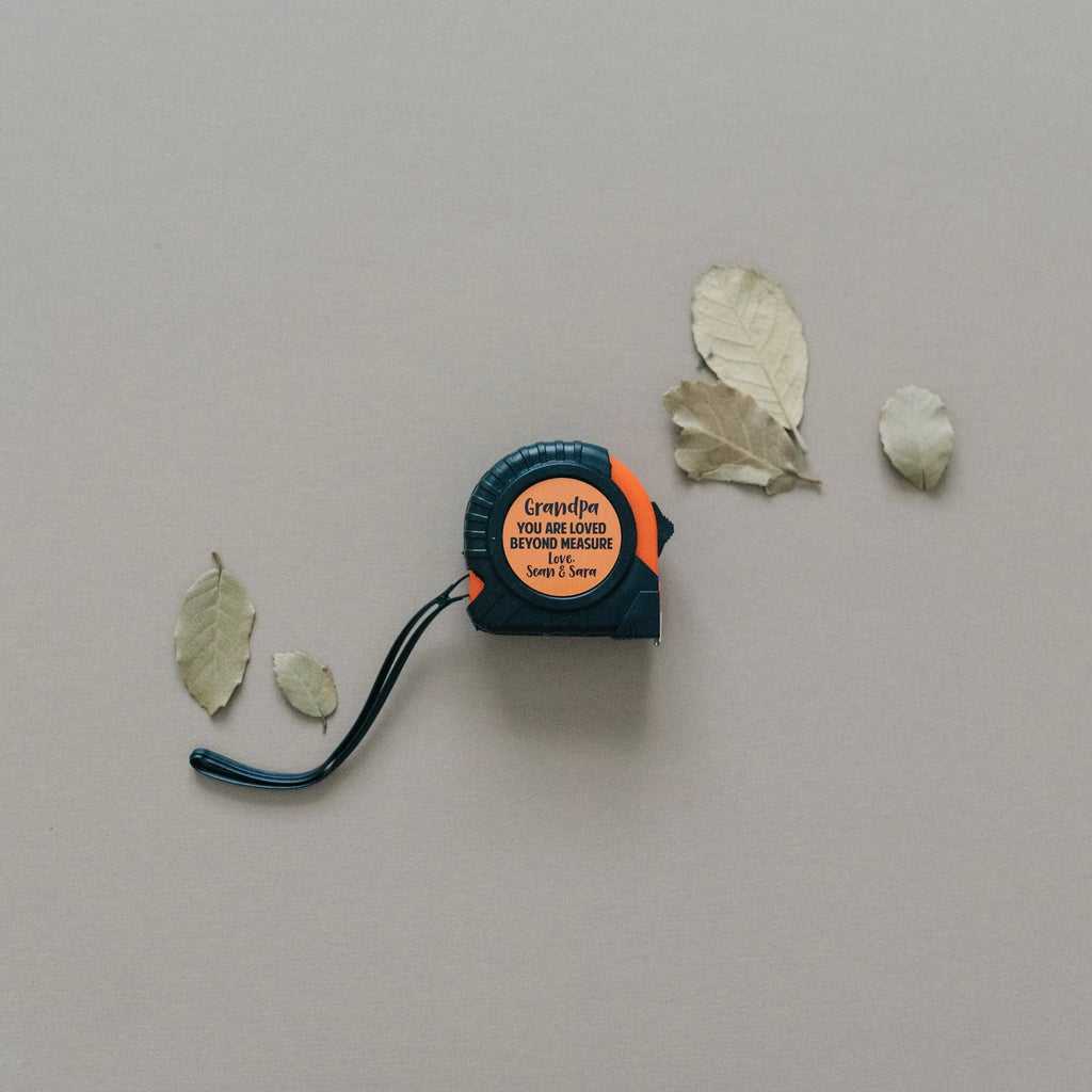 Personalized tape measure with round black housing, orange center label, and strap