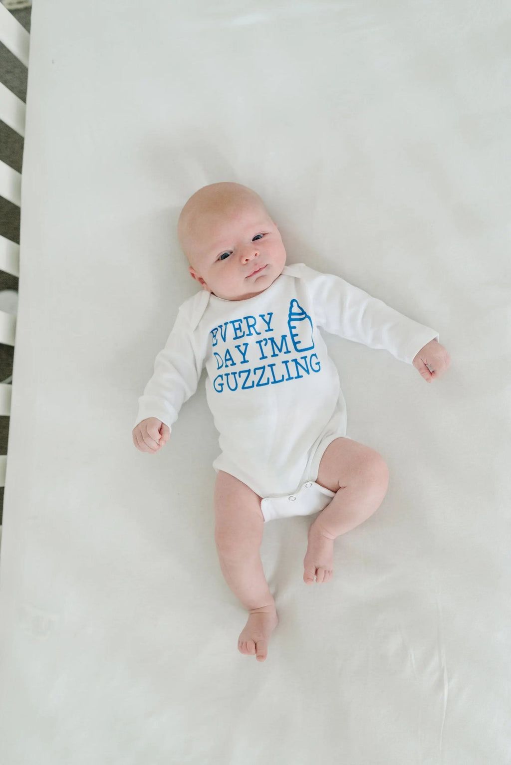 White newborn bodysuit with blue “Every Day I’m Guzzling” text, baby in it