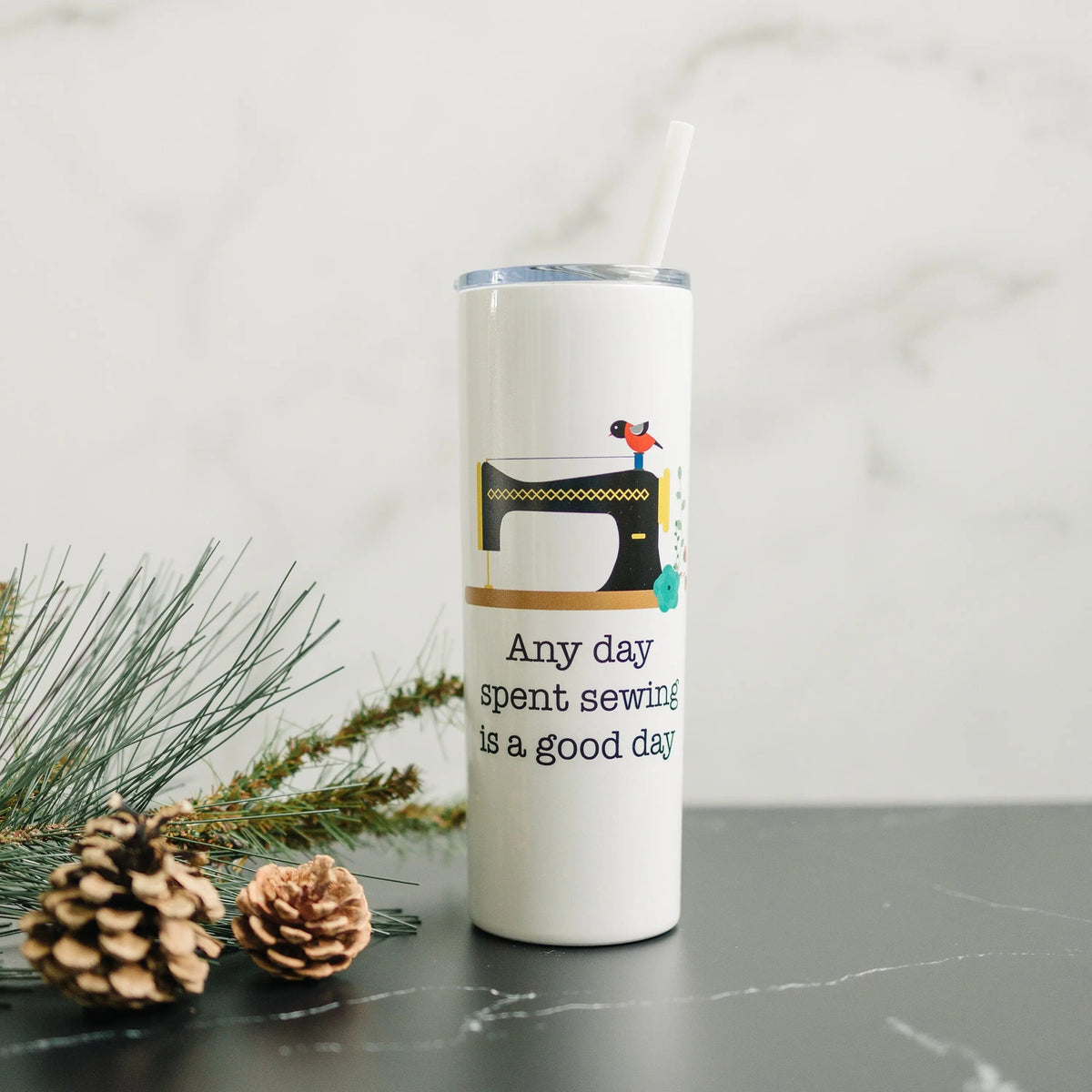 White skinny travel tumbler with straw, clear lid, and sewing machine quote graphic