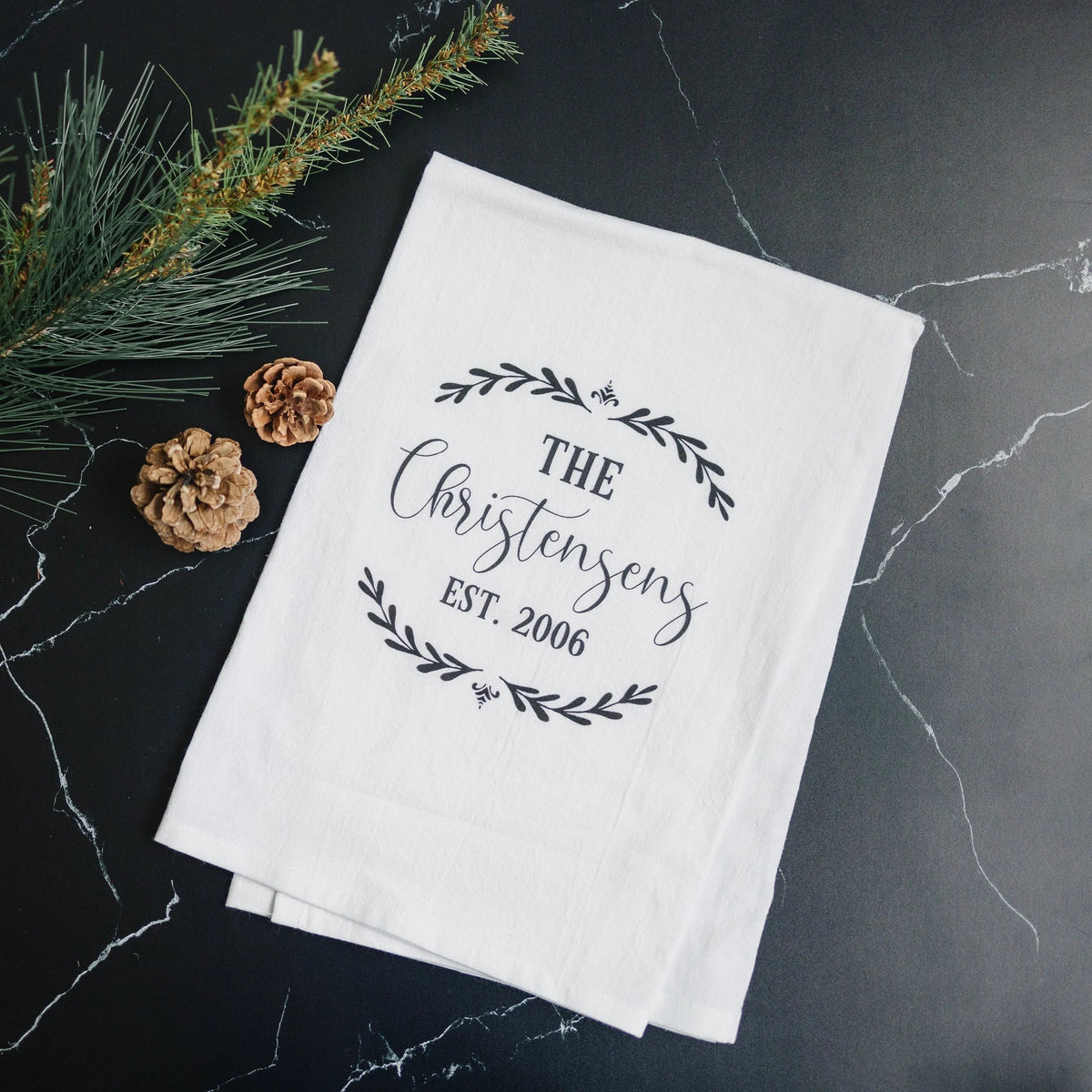 Folded white flour sack towel with wreath “The Christiansen Est. 2006” print