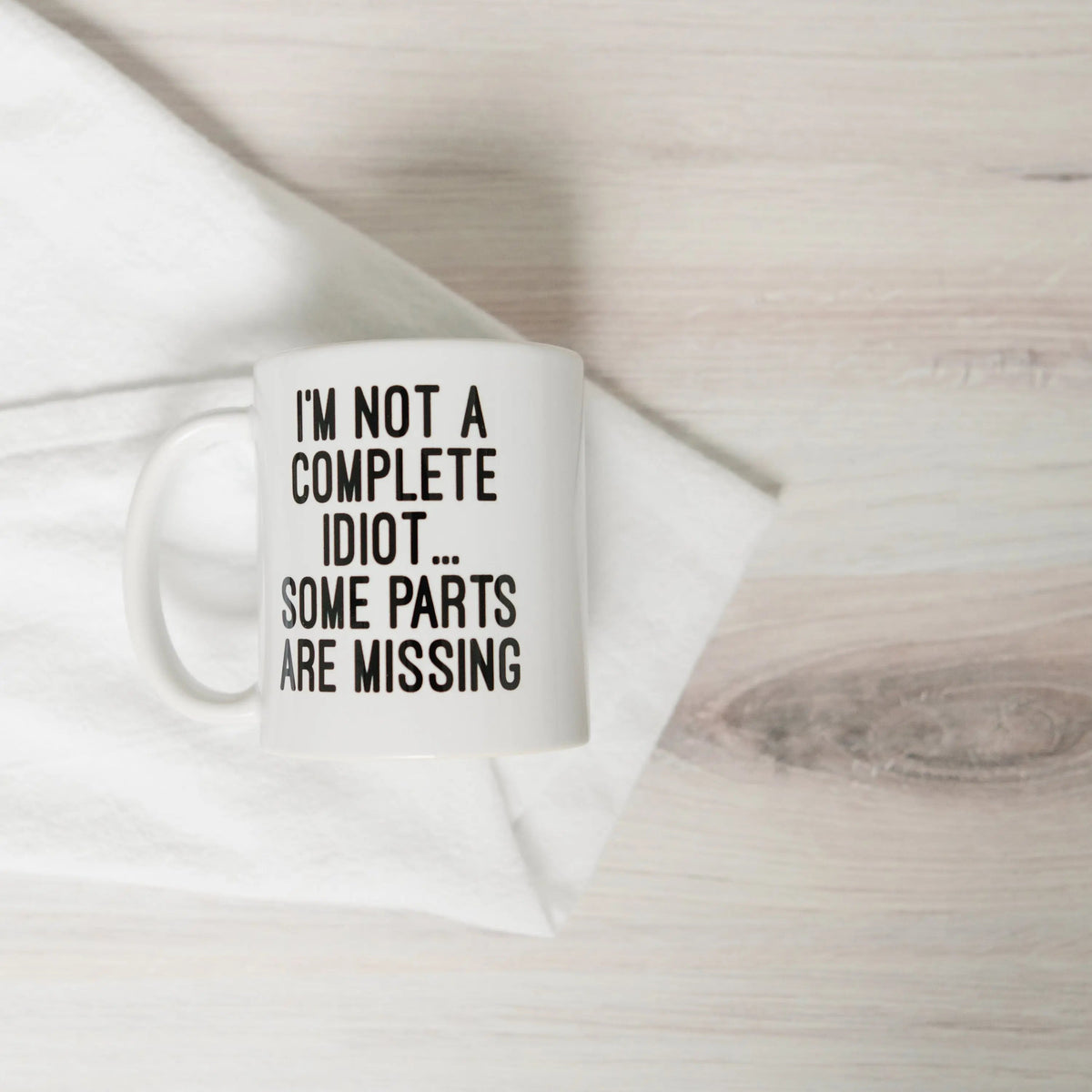 White ceramic coffee mug with quote "I'M NOT A COMPLETE IDIOT... SOME PARTS ARE MISSING"