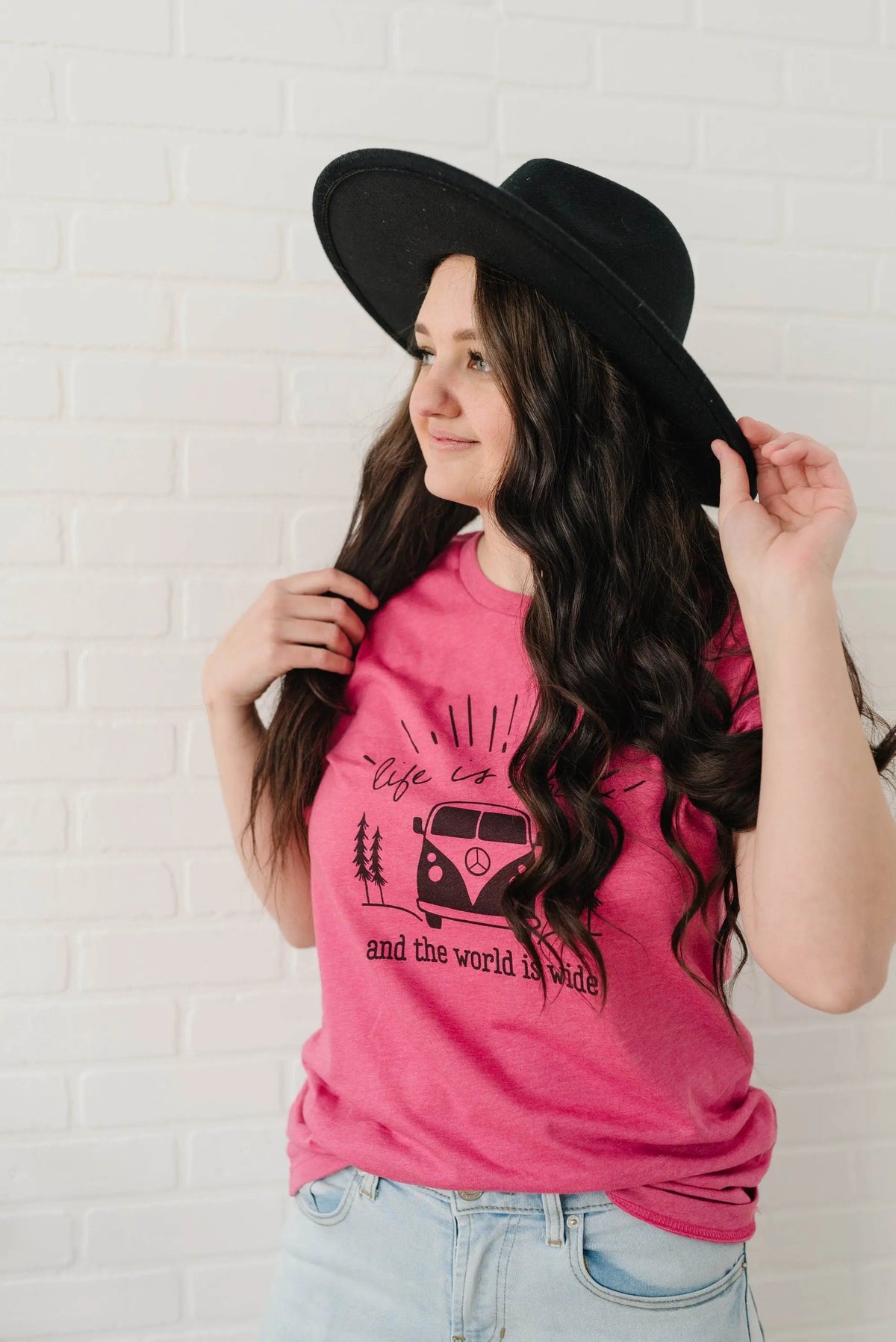 Women’s pink graphic t-shirt with camper van and trees graphic, on model wearing hat