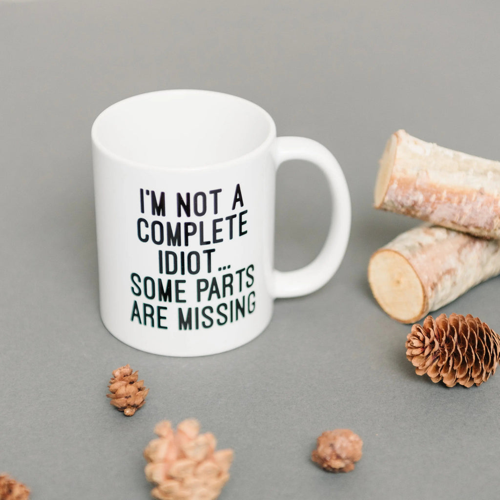 White ceramic coffee mug reading "I'M NOT A COMPLETE IDIOT... SOME PARTS ARE MISSING"