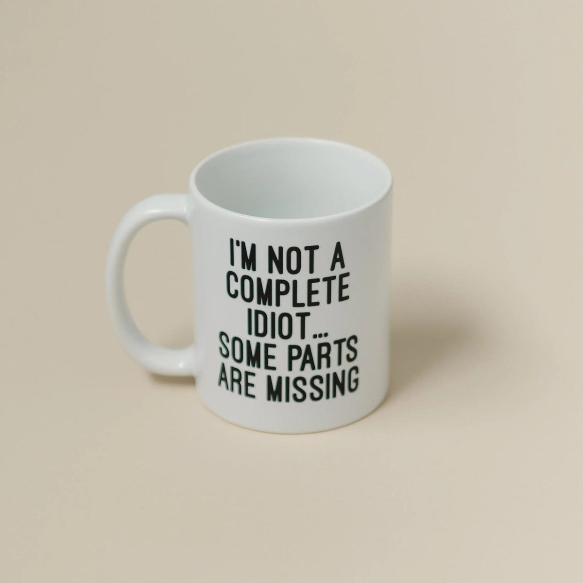 White ceramic coffee mug with text: "I'M NOT A COMPLETE IDIOT... SOME PARTS ARE MISSING"