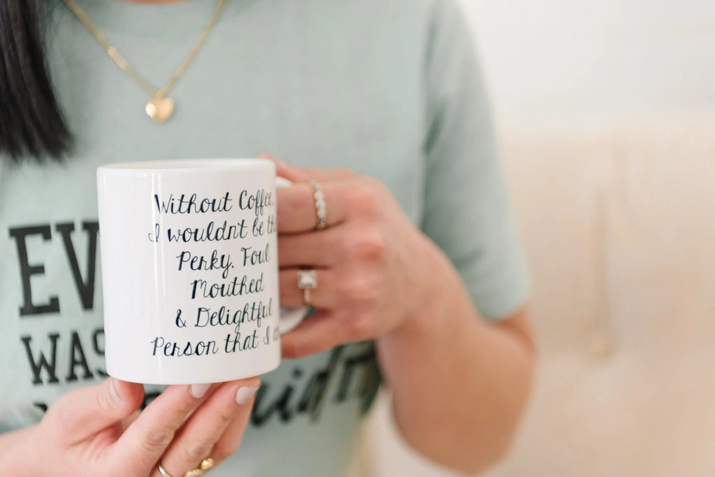 White ceramic coffee mug with black cursive quote, held in a person’s hand