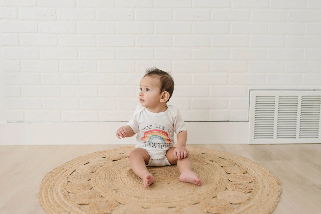 Baby wearing white rainbow “Sunshine” romper bodysuit, short sleeves, snap bottom