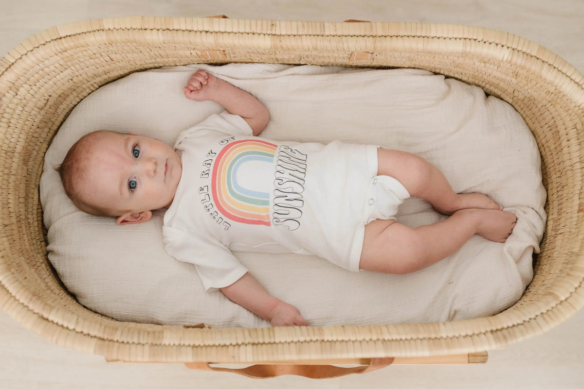Newborn lying in white rainbow “Sunshine” bodysuit with snaps, short sleeves