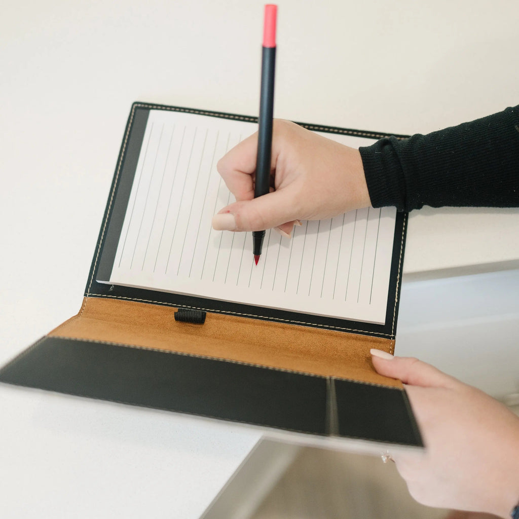 Hands writing on lined pages inside faux leather legal pad portfolio