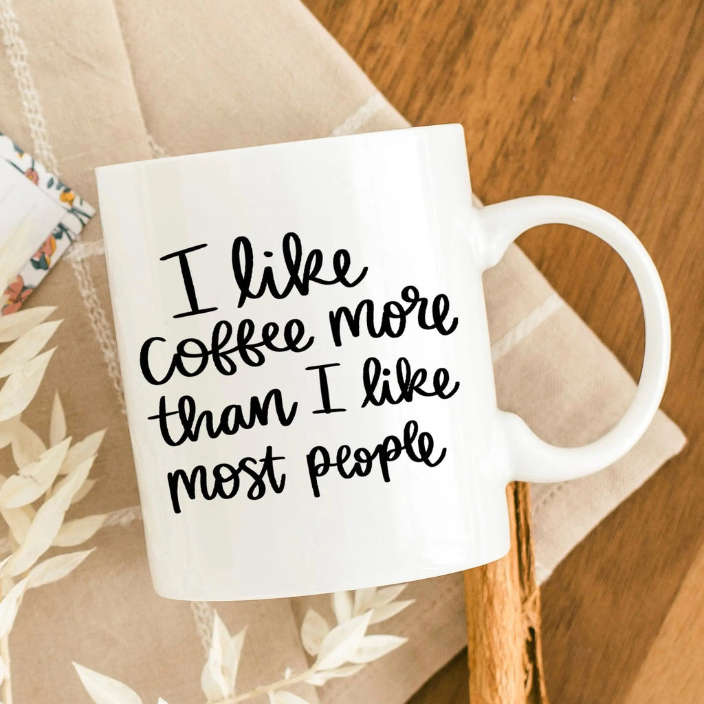 White coffee mug with black text: “I like coffee more than I like most people.”