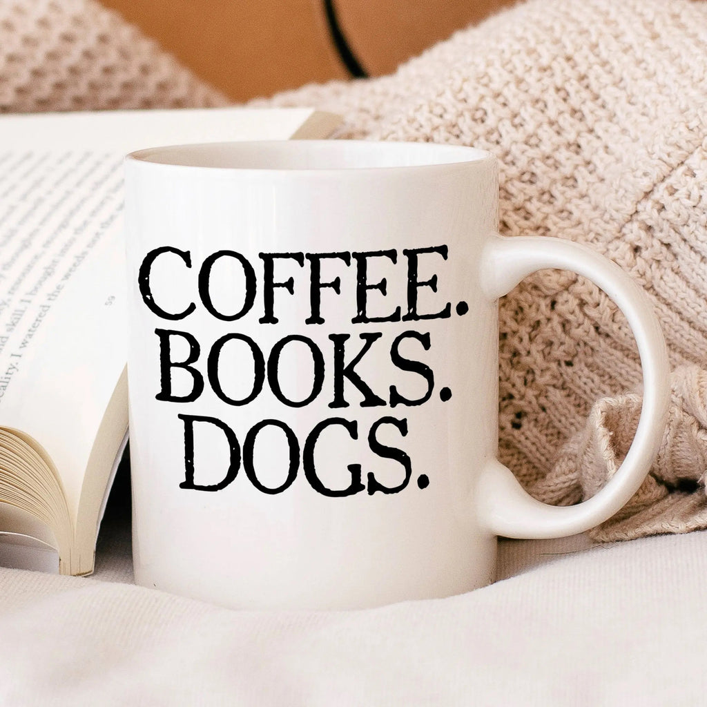 White ceramic coffee mug with 'COFFEE BOOKS DOGS' text and side handle