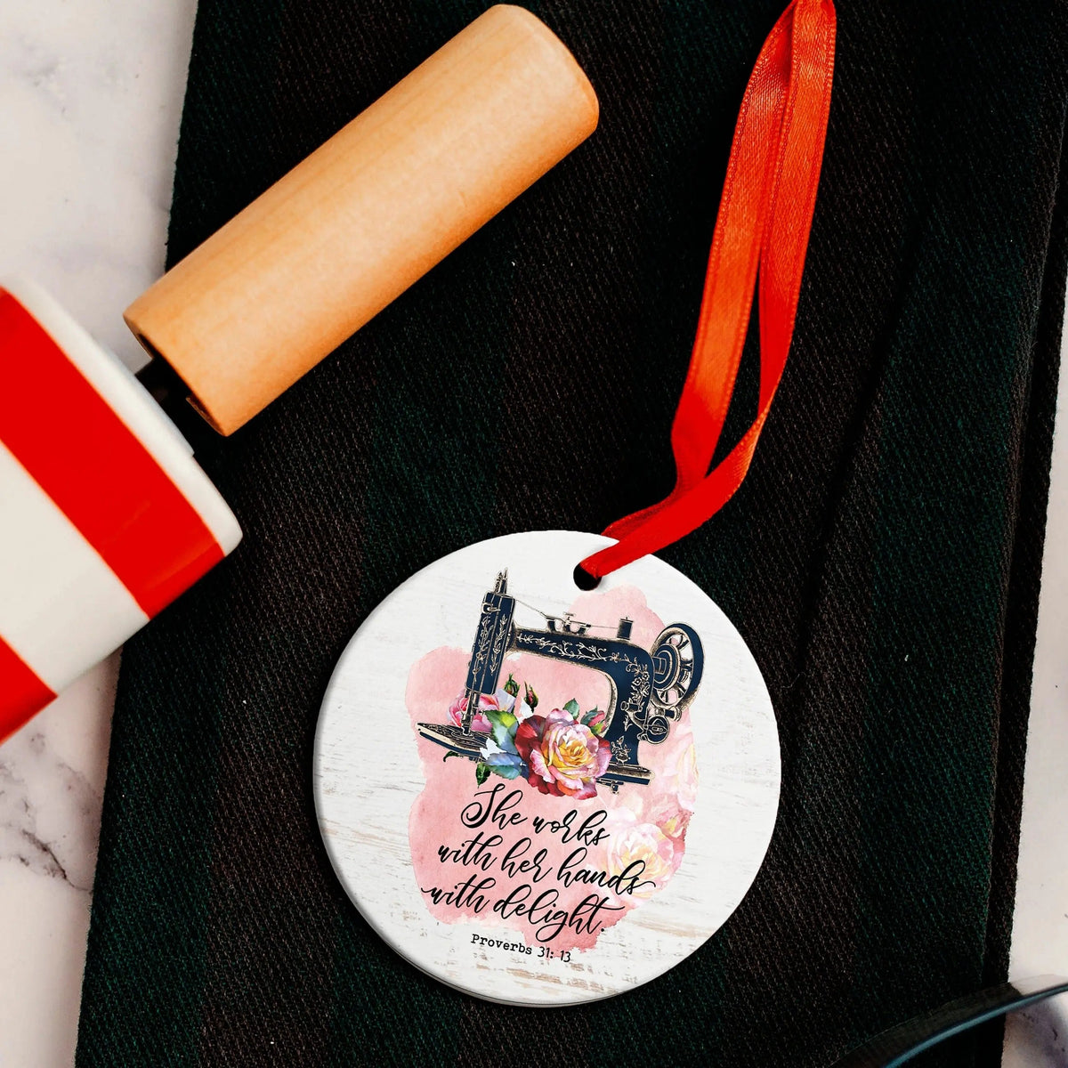 Round Bible verse ornament with sewing machine illustration and red hanging ribbon