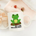 White ceramic coffee mug with green frog graphic and “Just a Girl Who Loves Frogs”