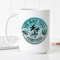 White ceramic coffee mug with teal beach logo, “The Beach Fixes Everything” graphic