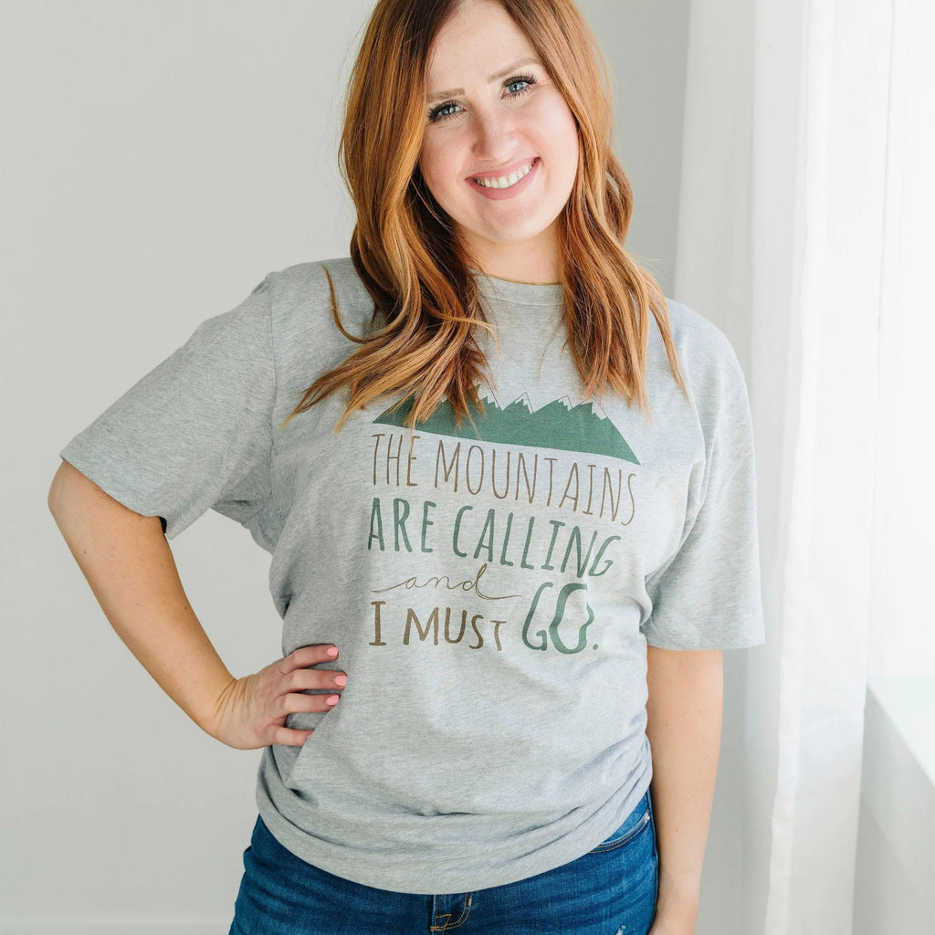 Gray crewneck unisex t-shirt with mountain graphic and "The Mountains are Calling" text