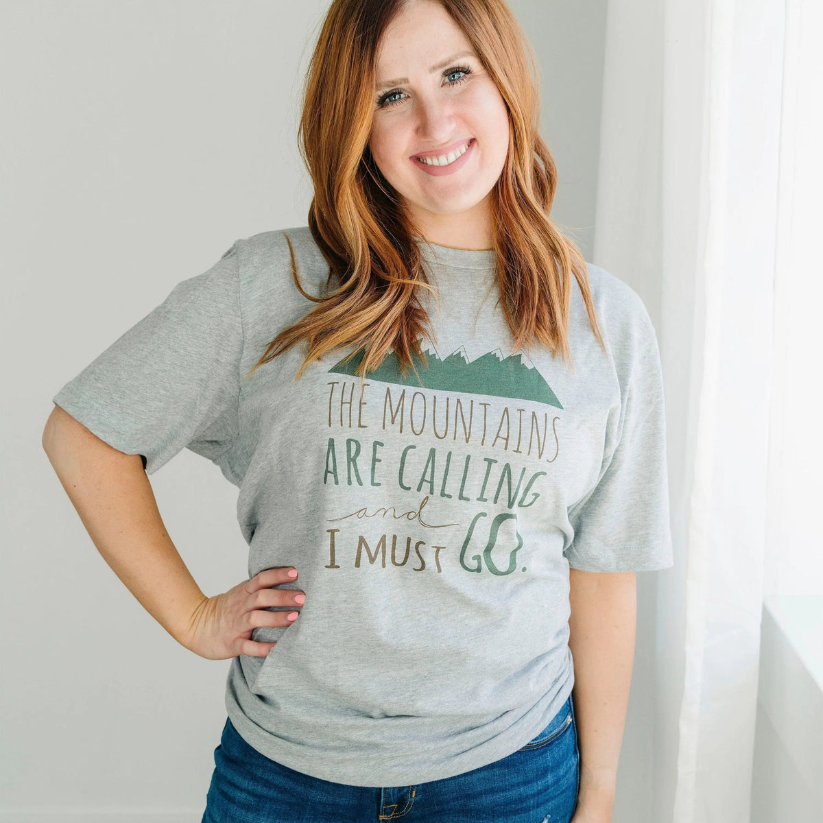 Gray crewneck unisex t-shirt with mountain graphic and "The Mountains are Calling" text
