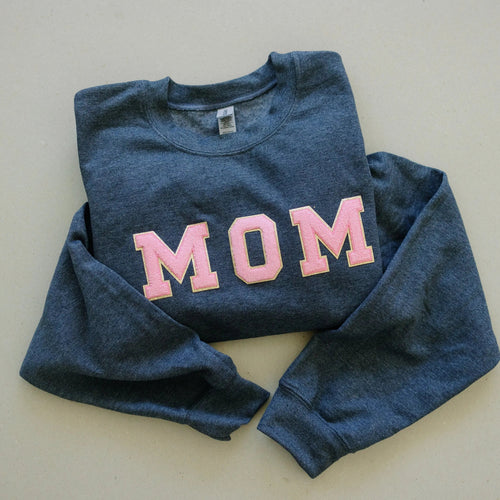 Dark gray crewneck sweatshirt with pink MOM chenille-style patch, laid flat