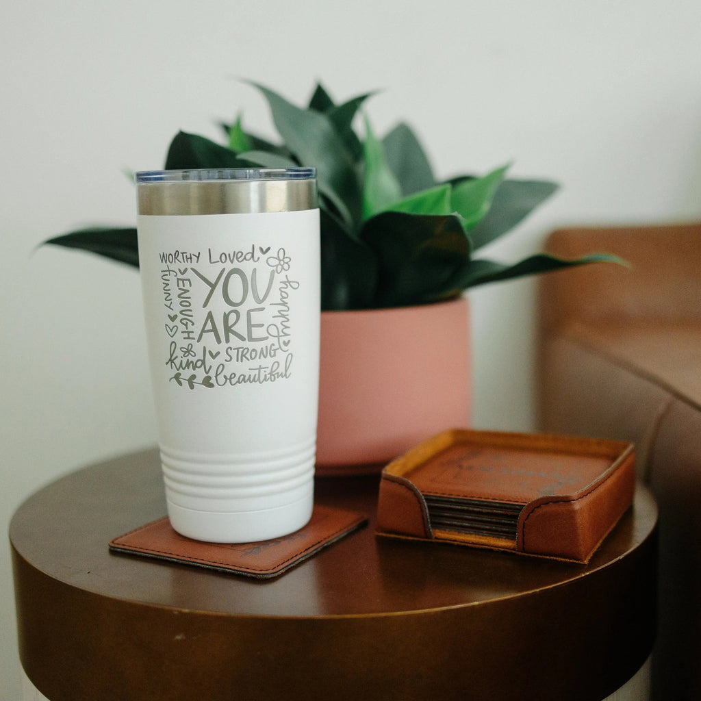 White inspirational tumbler with motivational quote, placed on a tabletop with coasters.