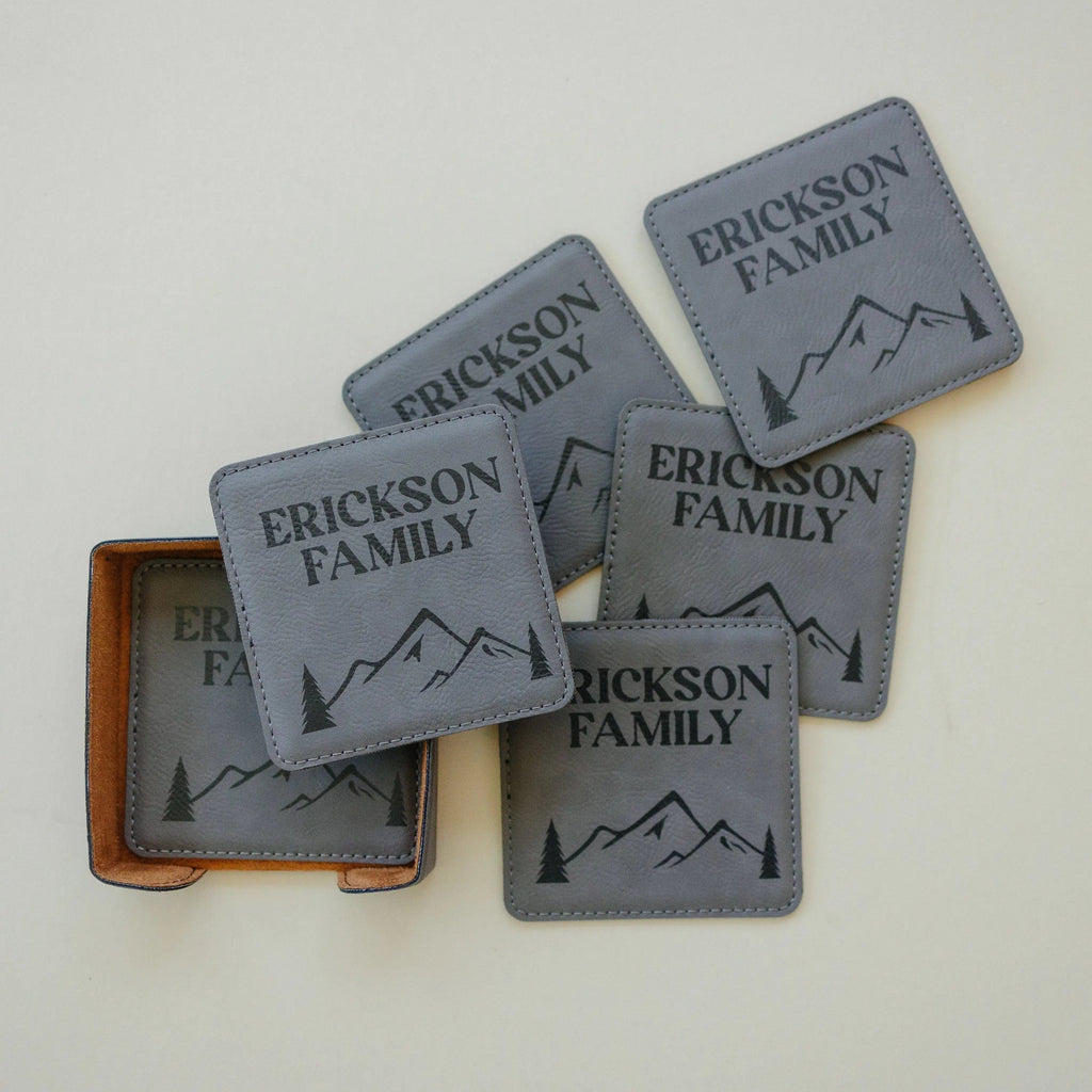 Personalized leather-look coasters in light gray with mountain silhouette and family name