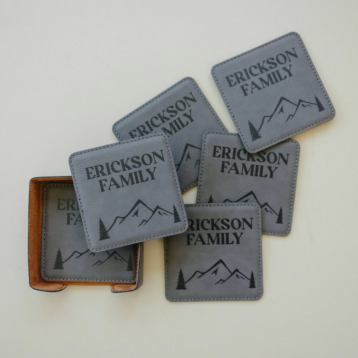 Personalized leather-look coasters in light gray with mountain silhouette and family name