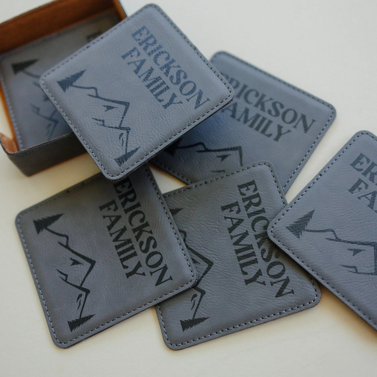 Assorted light gray leather-look coasters with ERICKSON FAMILY text and mountain graphic