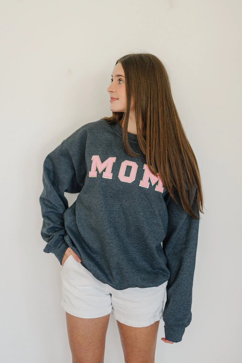 Dark gray crewneck sweatshirt with pink MOM patch, model viewed from back