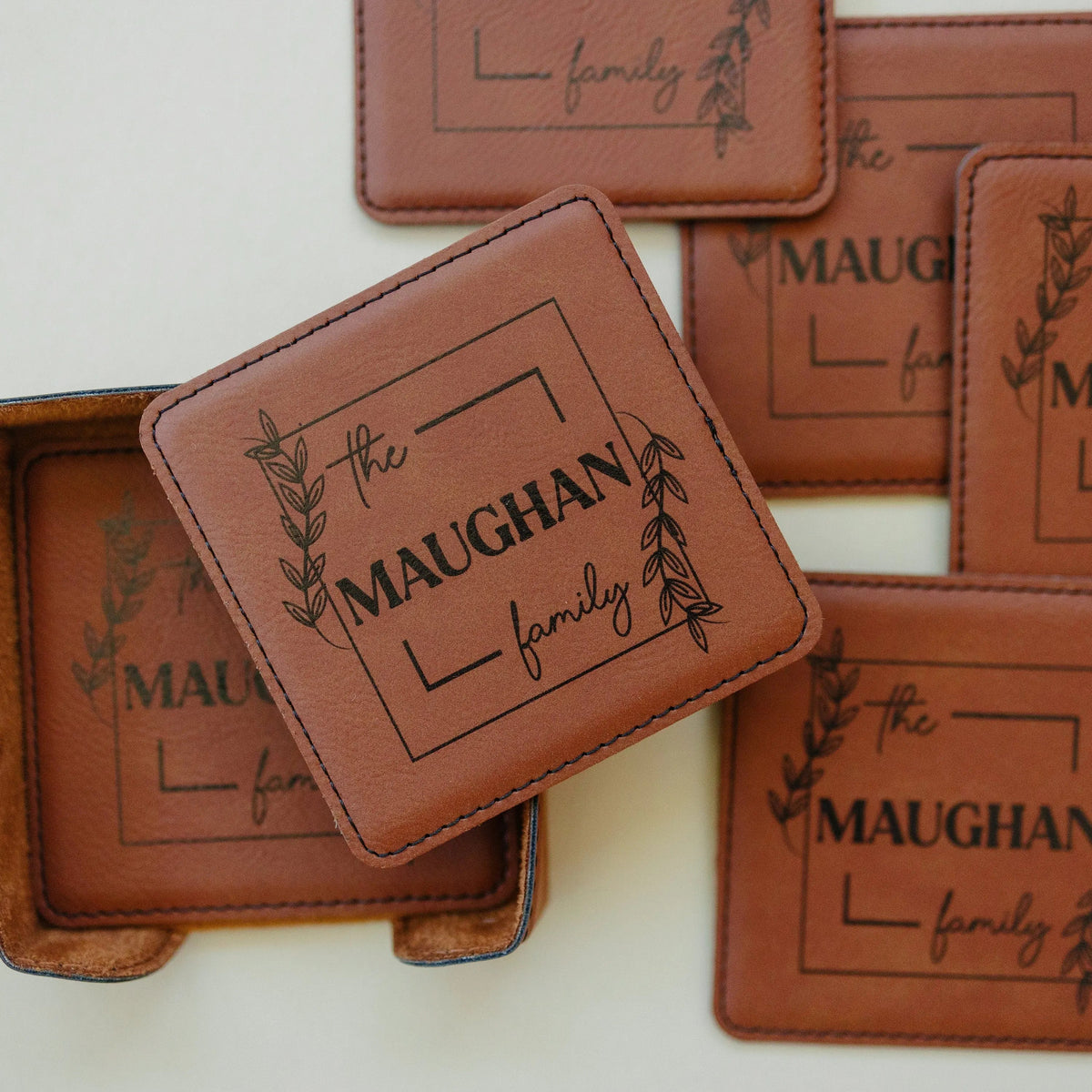 Close-up of warm brown leather-look coasters with MAUGHAN family text and leaf wreath