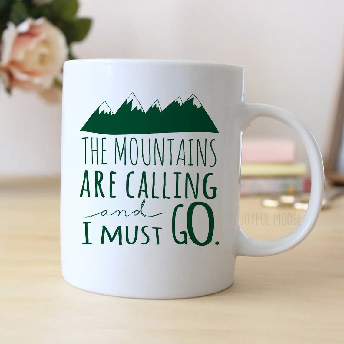 White ceramic mug with green mountain graphic and quote text on front