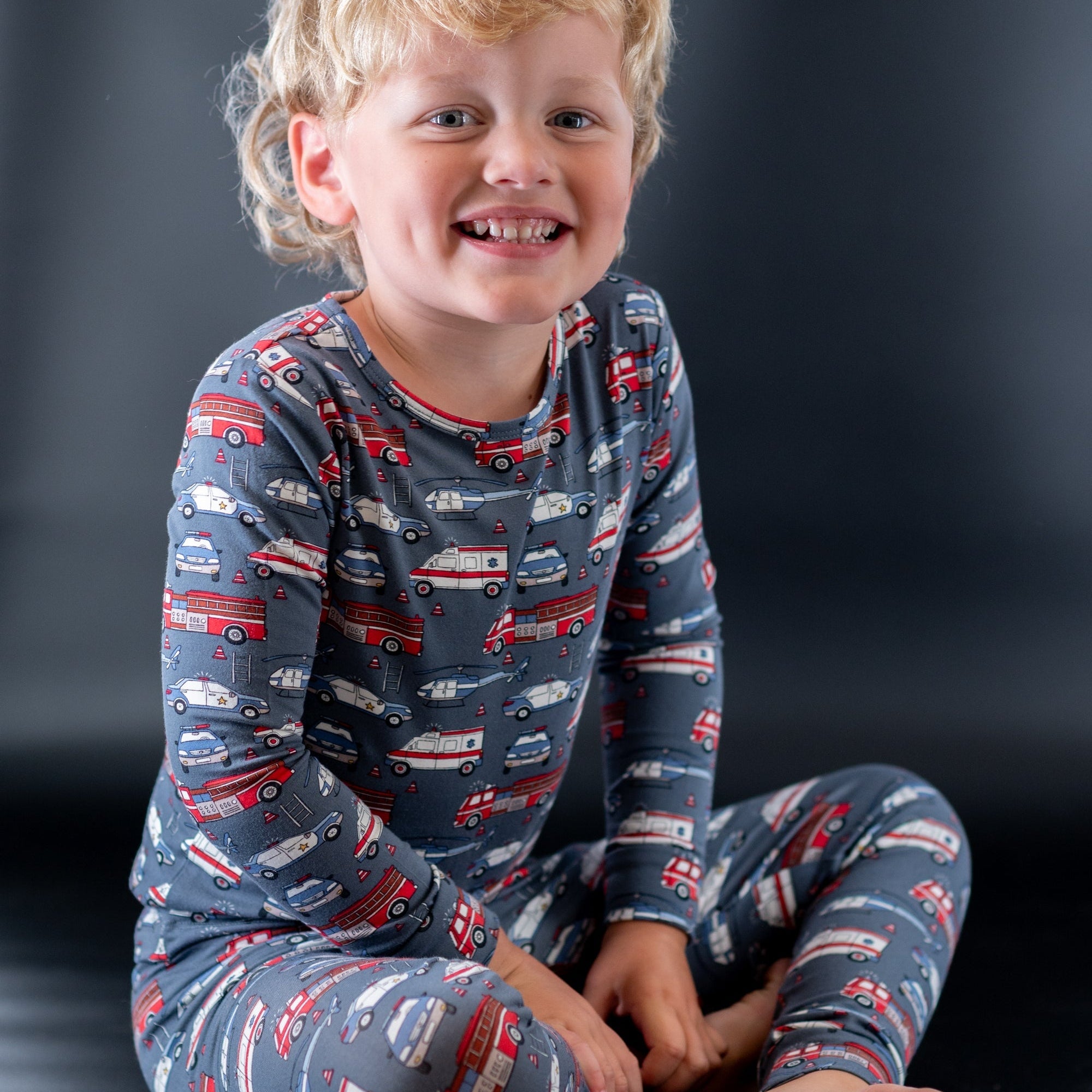 Kids long-sleeve pajamas in navy truck print, smiling child seated