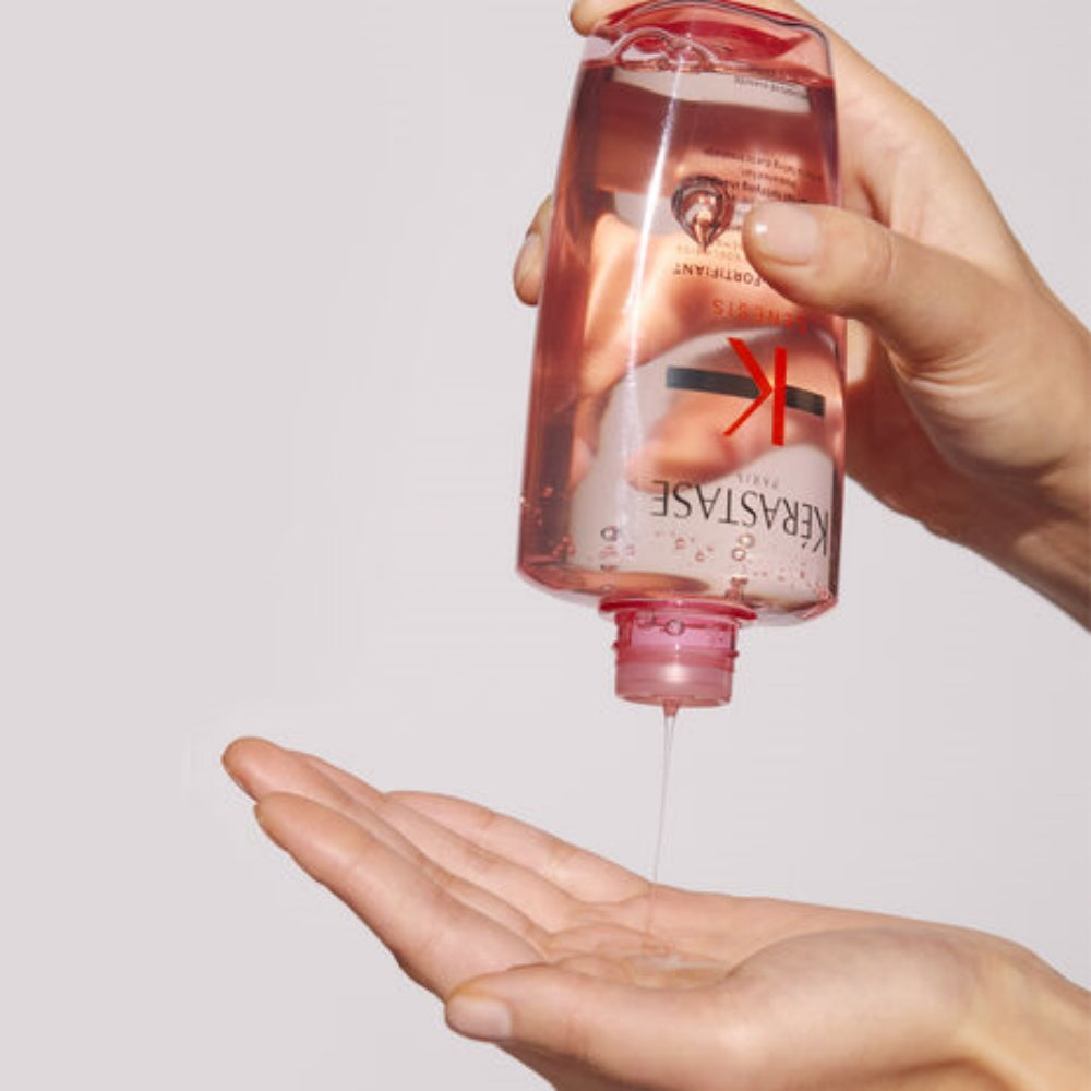 Hand holding Kérastase Genesis shampoo bottle with droplets and red label markings