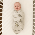 Baby swaddle blanket in cream with green dinosaur print, newborn wrapped