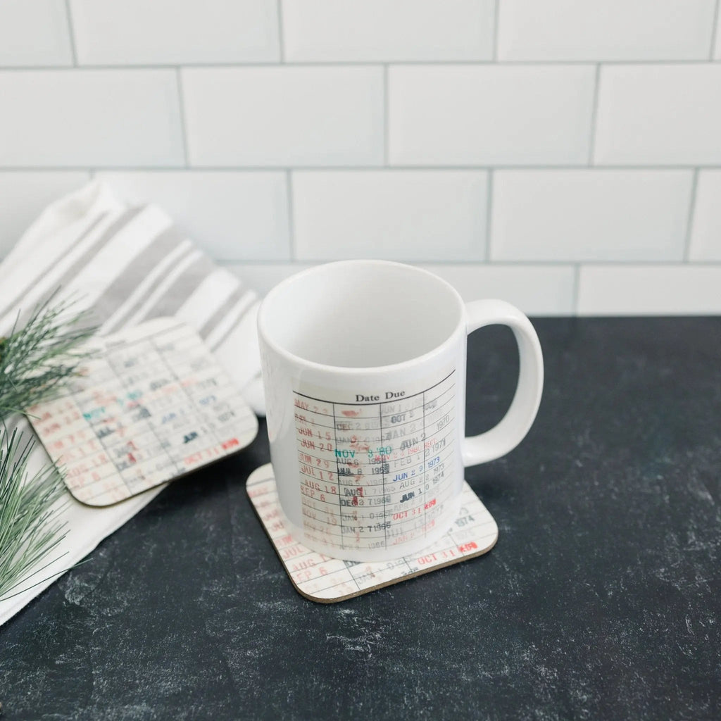 White coffee mug with date-due calendar print on coaster with folded book