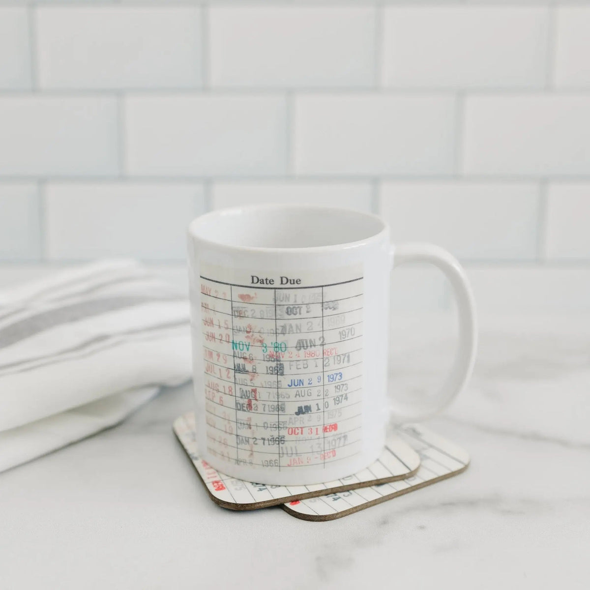 White coffee mug with date-due calendar print on coaster against light wall