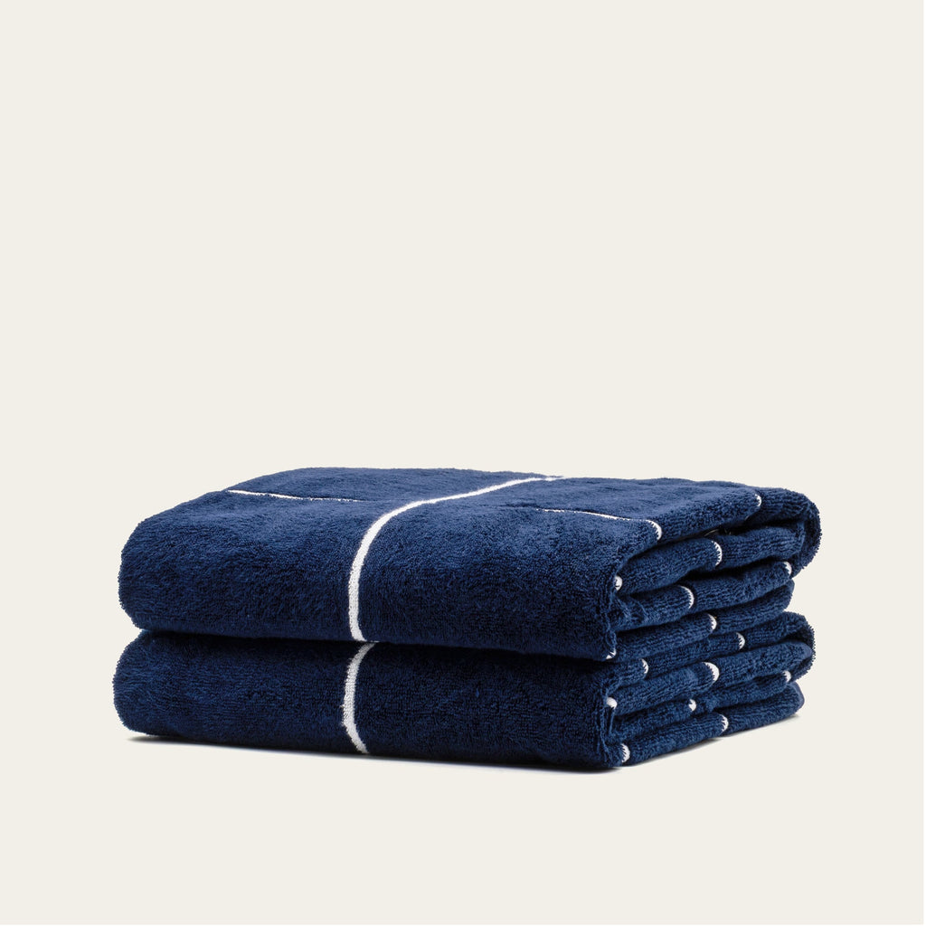 Rolled navy cotton towel with white stripe band, stacked with a second towel