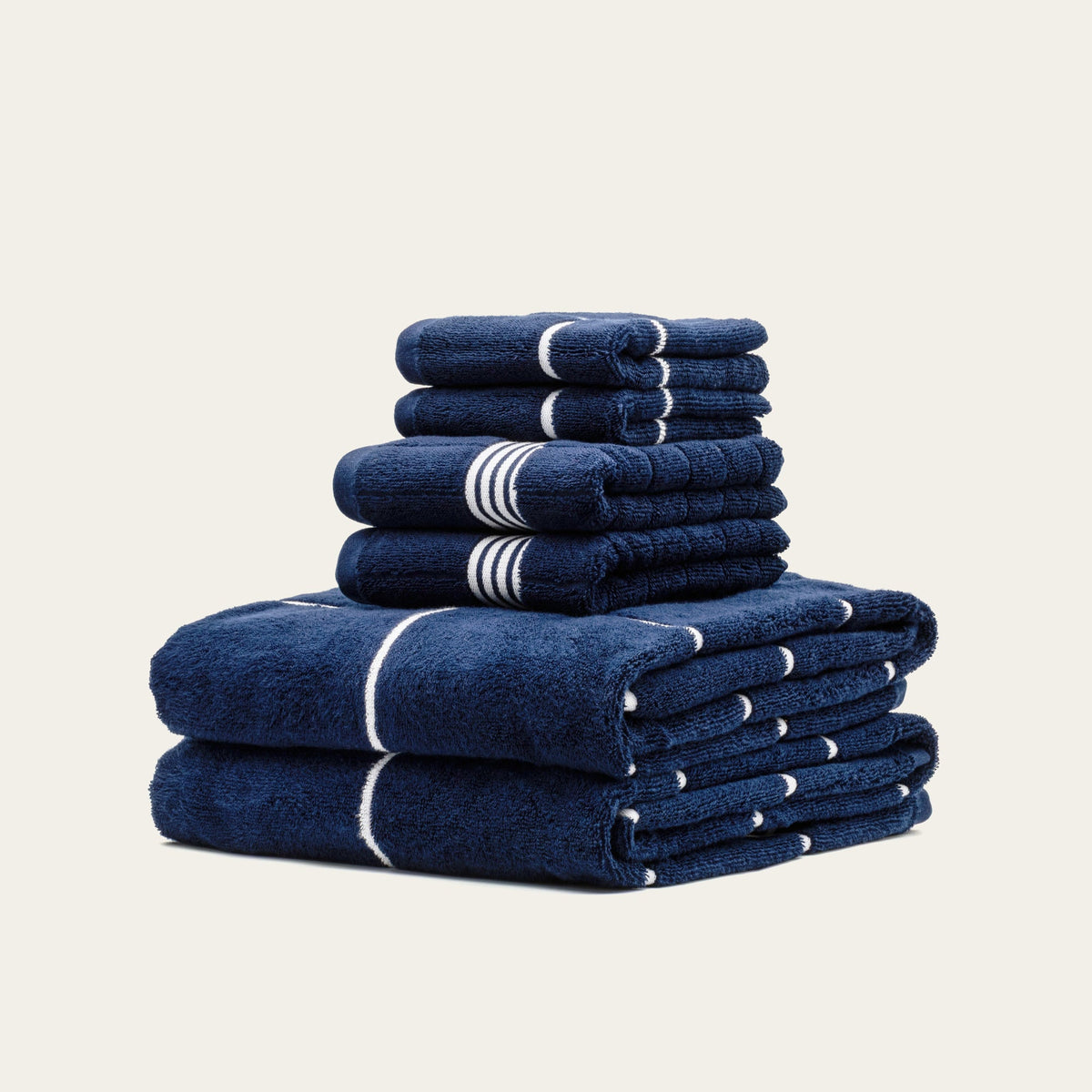 Navy cotton towel set with white stripe bands, folded into stacked piles