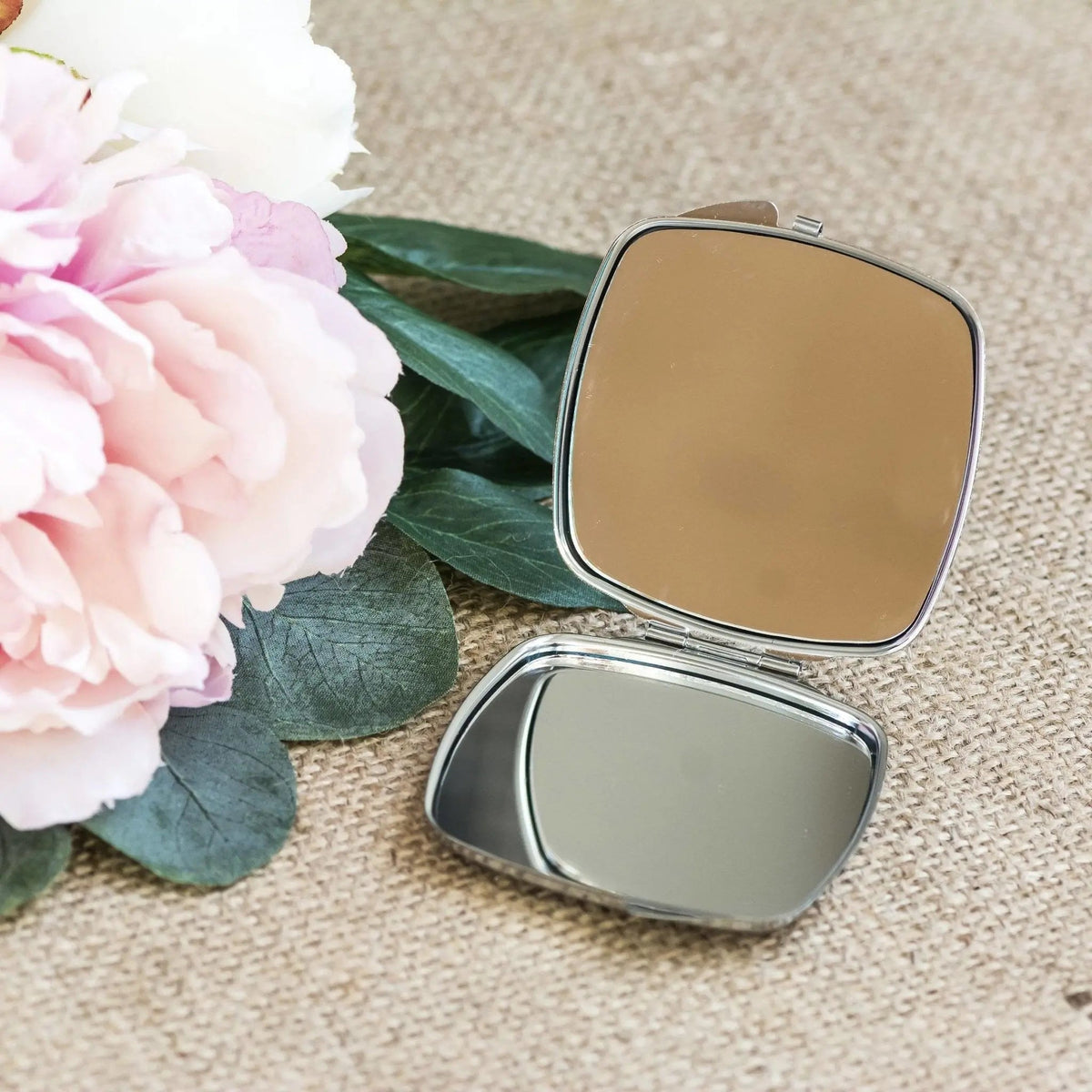 Silver double-compartment compact mirror, open, showing one blank reflective panel.