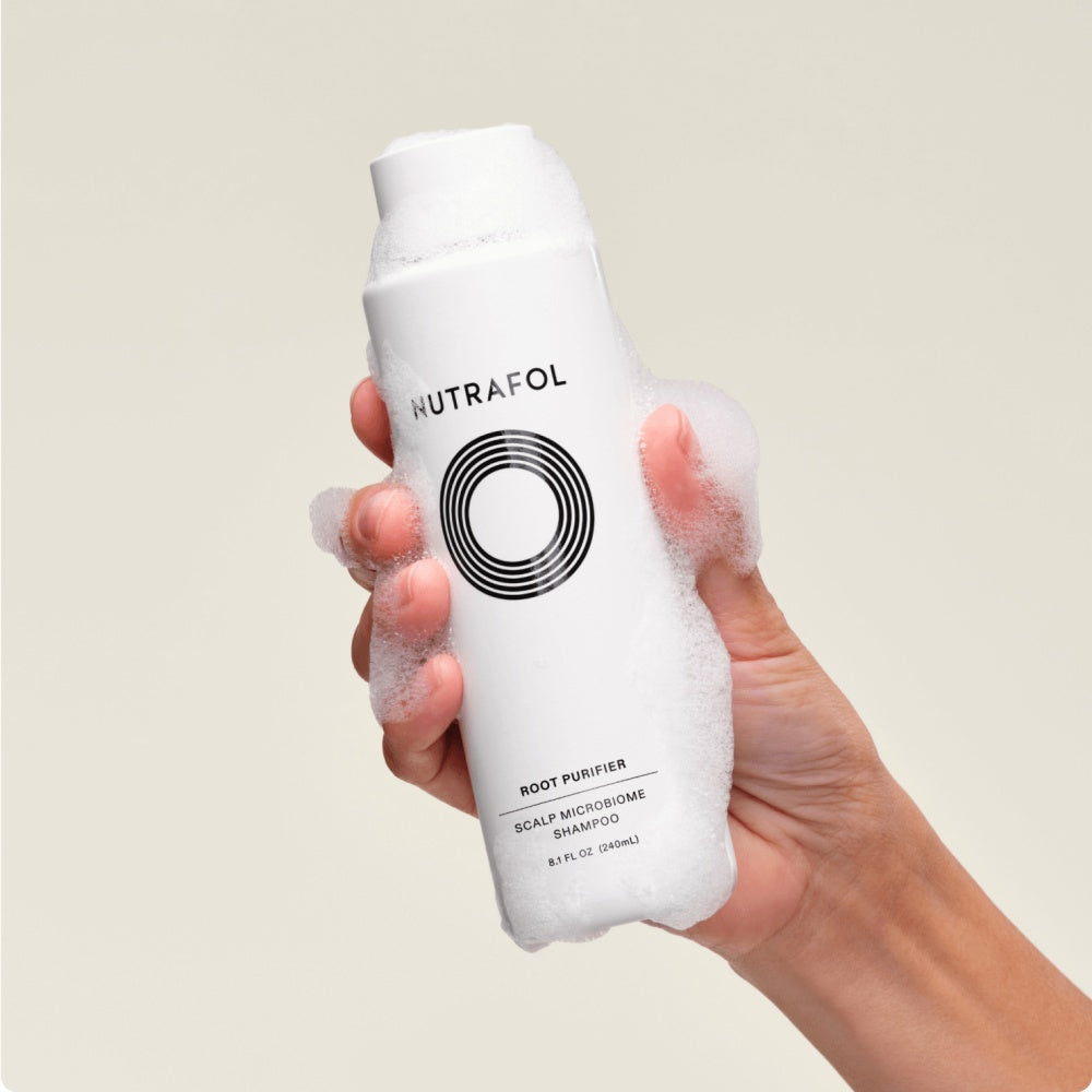 Nutrafol Root Purifier shampoo bottle held in hand, white bottle with black circular logo