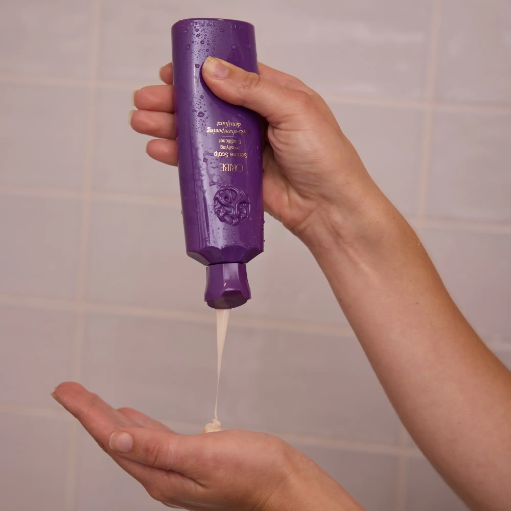 Purple conditioner bottle dispensing a clear stream into an open palm