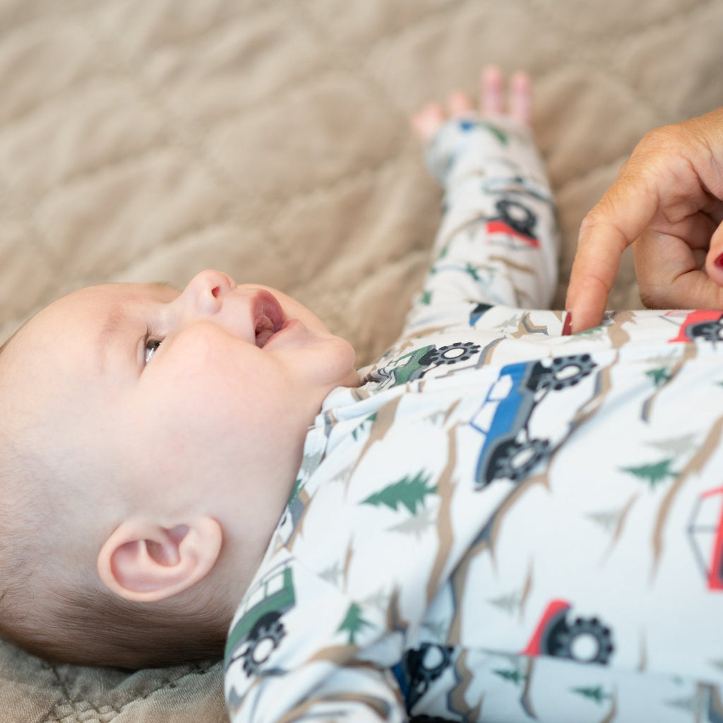 Baby zipper footie in white with colorful vehicles and evergreen tree pattern, close-up